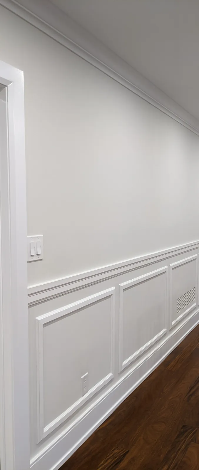 White picture-frame wainscoting below a chair rail along a dining room wall, with crown moulding above