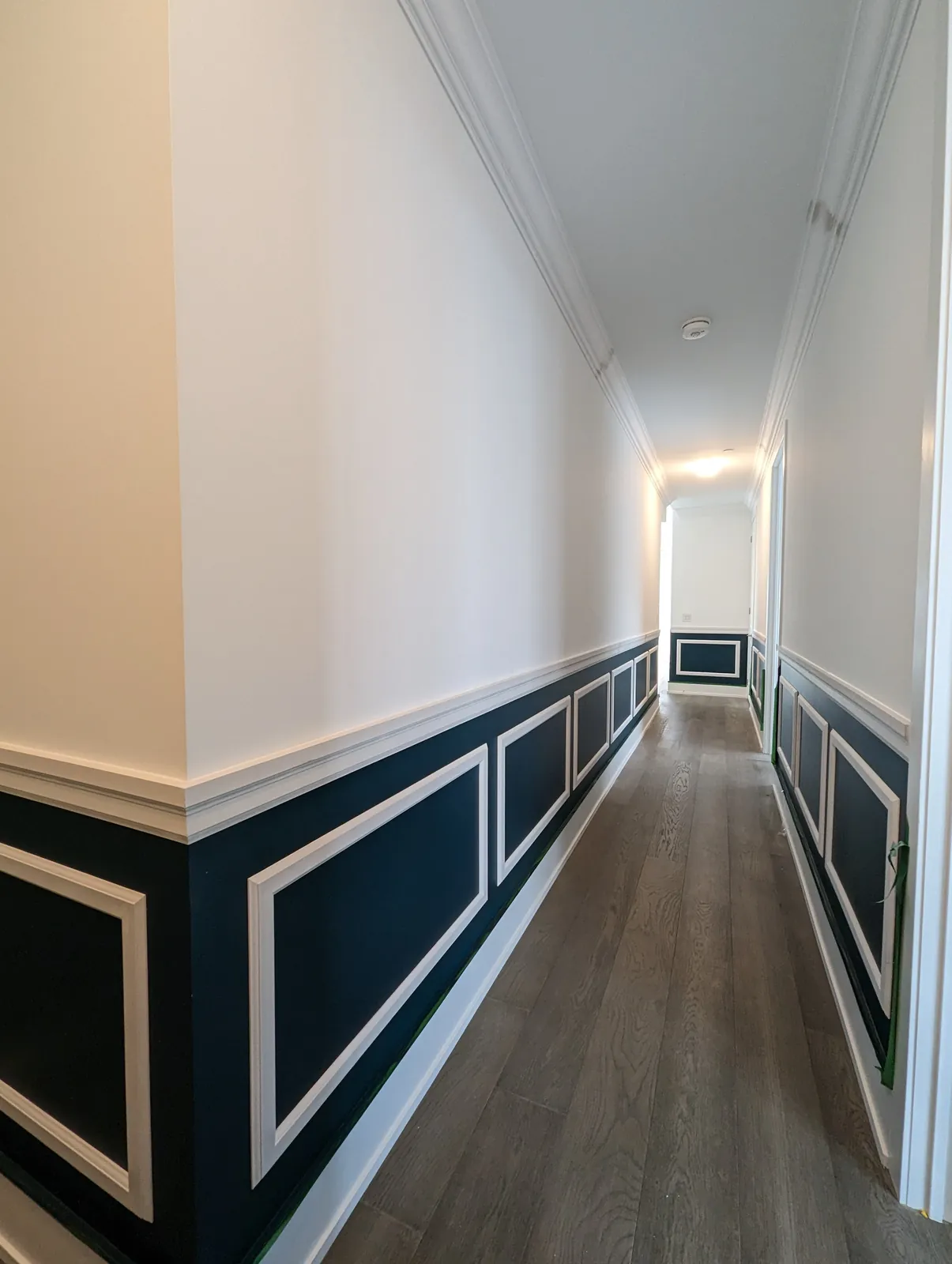 Navy hallway with white chair rail wainscoting, picture frame panels below the rail and crown moulding