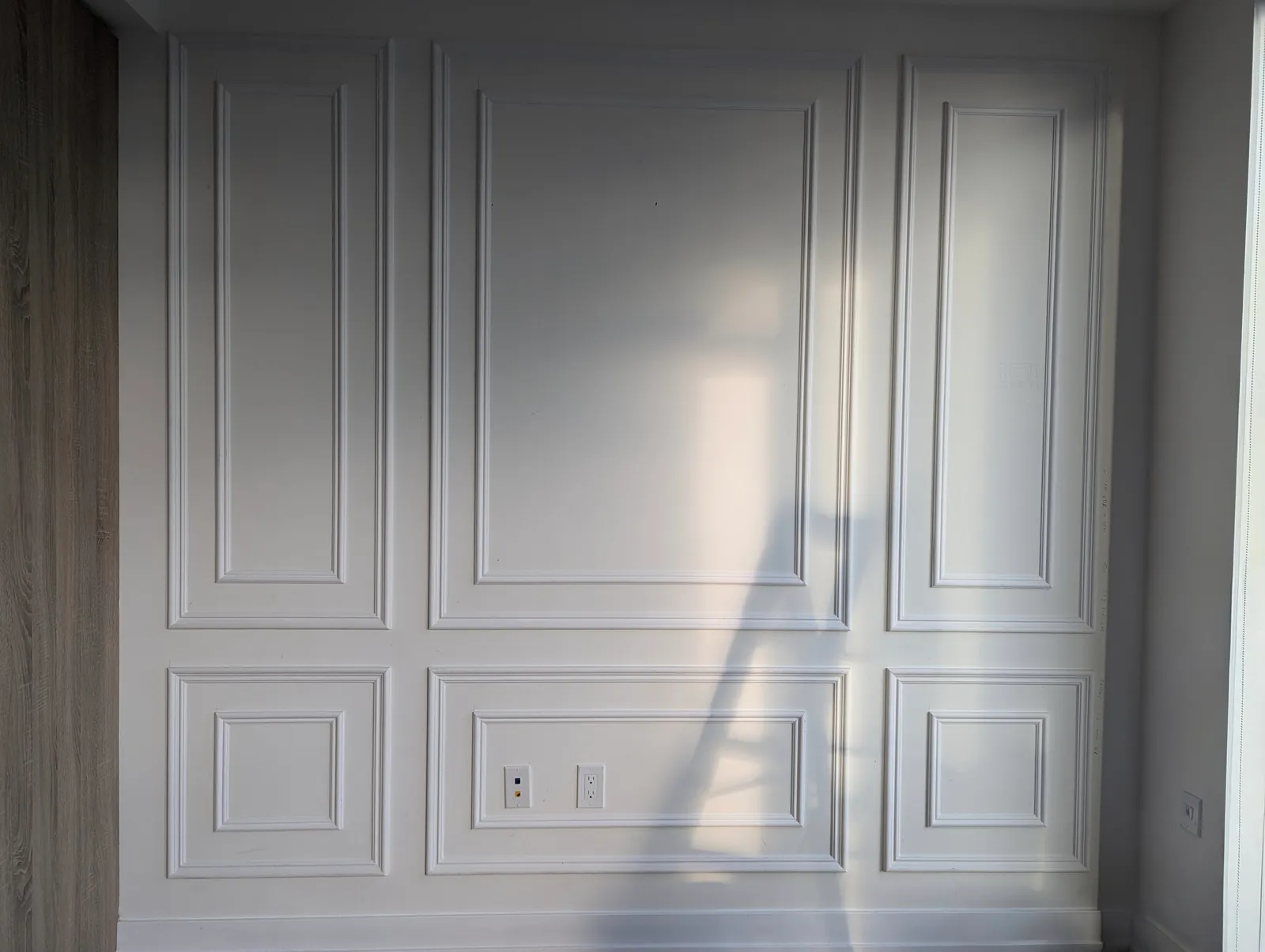 White wall with two rows of double picture-frame panels, crossed by a diagonal band of sunlight