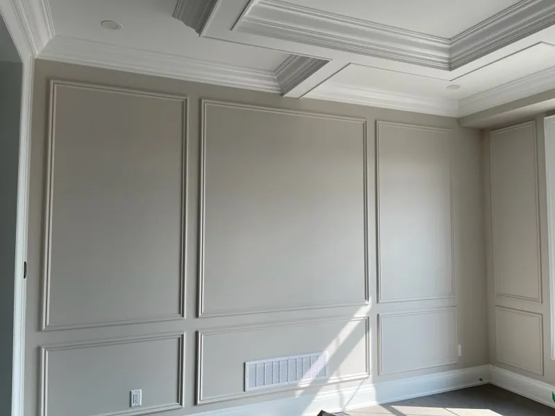 Empty room with two rows of greige picture-frame wall panels under a coffered ceiling with crown moulding